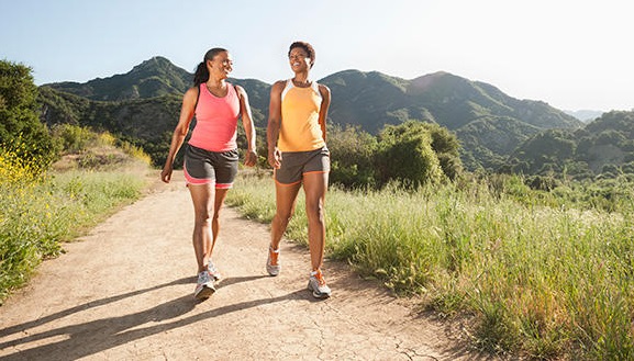 2 women walking on a hiking path with mountains in the background