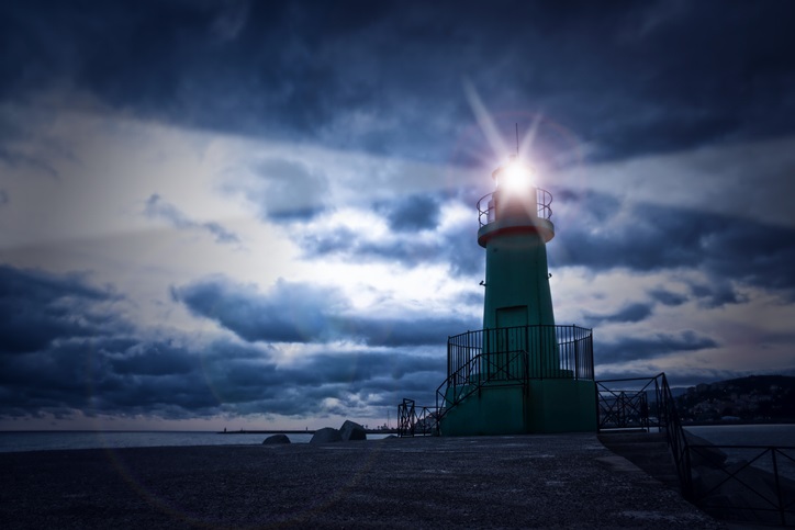 A lighthouse with a bright light shining through a cloudy sky