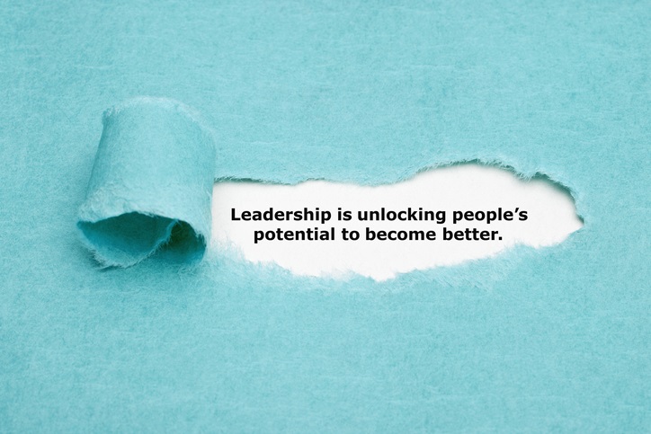 A background of blue paper with a piece in the middle torn away, revealing the words "Leadership is unlocking people's potential to become better."