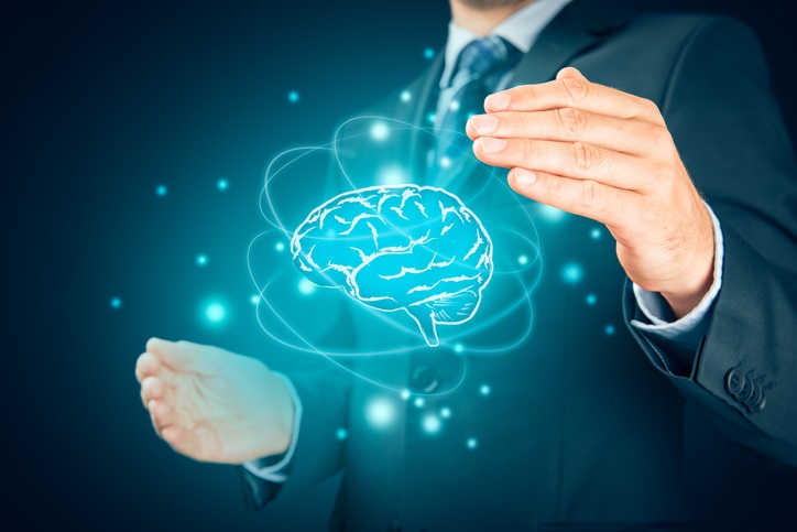 The image shows a man in a suit holding his hands around a glowing, holographic brain. The brain is stylized in blue, surrounded by orbital-like lines and floating particles, giving it a futuristic or digital appearance.