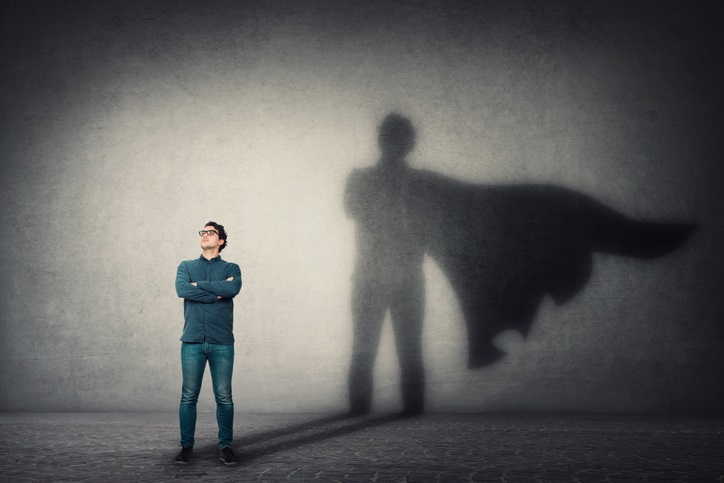 Photo of a man standing with his arms crossed, his shadow cast on a wall behind him has the addition of a superhero cape