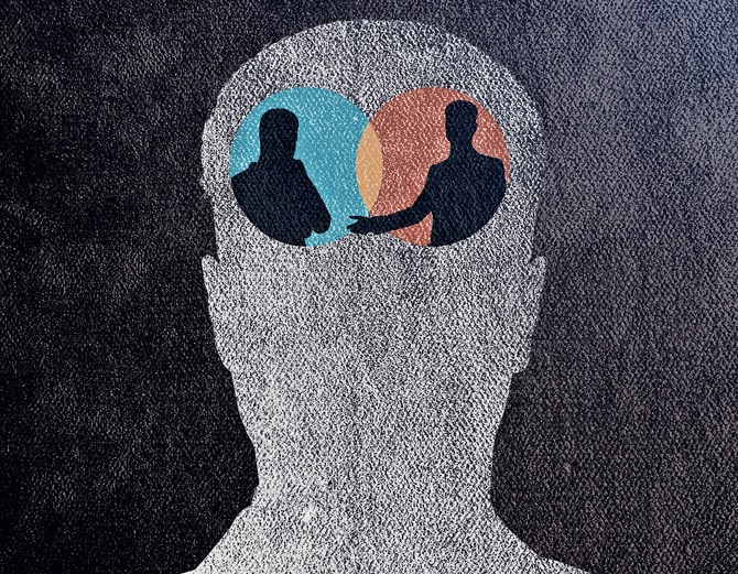 The outline of a human head with two silhouetted figures facing each other within the head, located where the brain would be. Each silhouette is set within a colored circle — one blue (left), the other orange/red (right) — with a small overlapping area in the center (reminiscent of a Venn diagram).