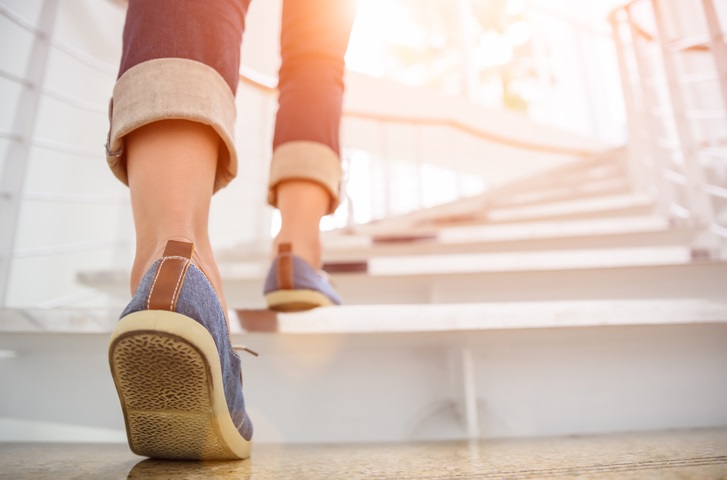 A person putting their right foot onto the first step of a staircase