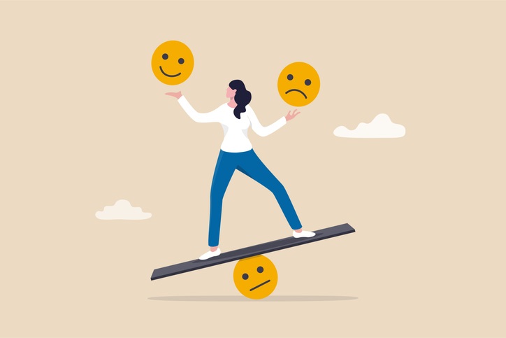 Cartoon of a woman standing on a beam trying to balance while holding a smiley face in one hand and a sad face in the other